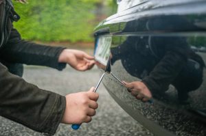 A person steals the license plate on a car with a screwdriver